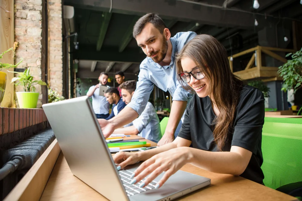 Mujer con lentes y un compa&ntilde;ero trabajando juntos en un computador port&aacute;til