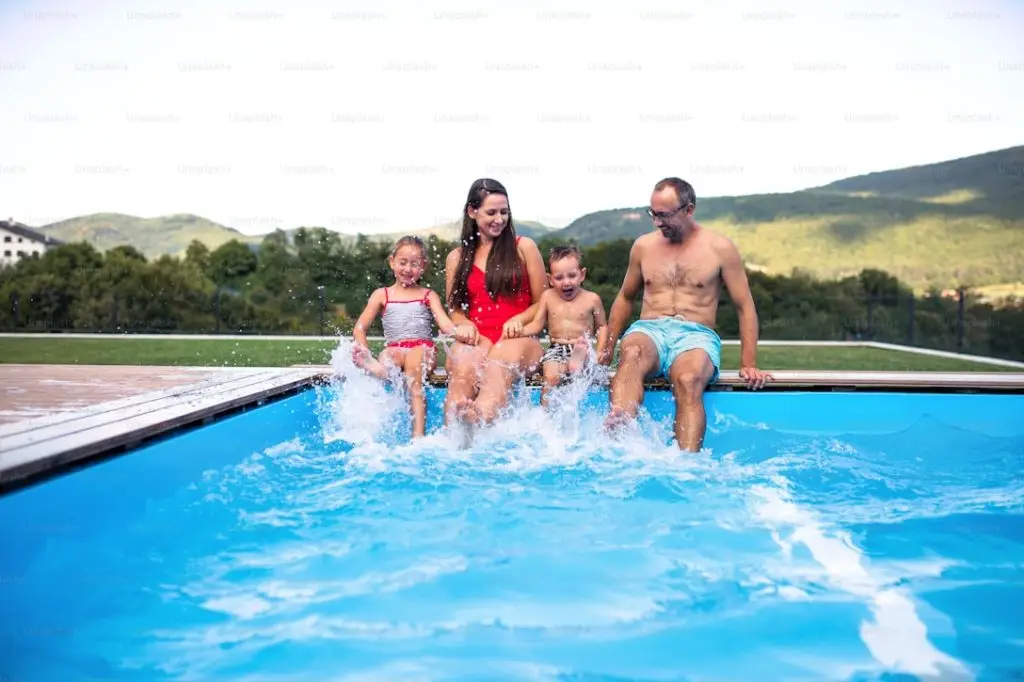 Familia sentada en el borde de una piscina salpicando agua con los pies