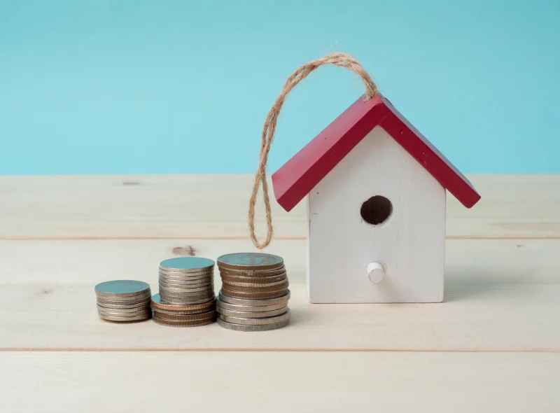 Casa de juguete con techo rojo junto a pilas de monedas