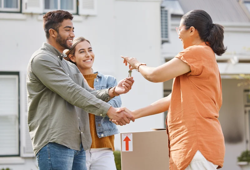 Pareja recibiendo las llaves de su casa mientras estrecha la mano de la asesora