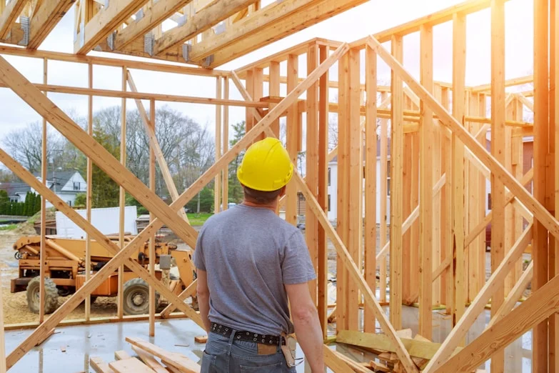 Obrero con casco amarillo frente a la estructura de madera de una casa en construcci&oacute;n