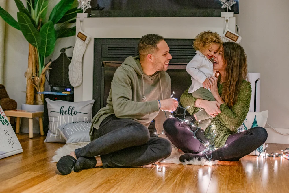 Familia riendo sentada en el piso de su sala junto a la chimenea