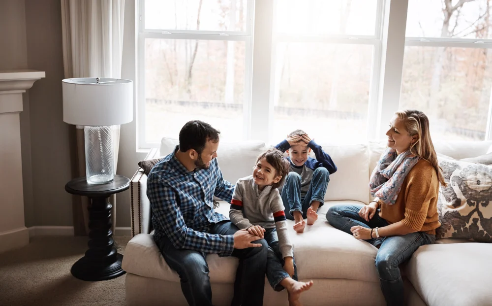 Familia con dos hijos riendo en el sof&aacute; de su sala
