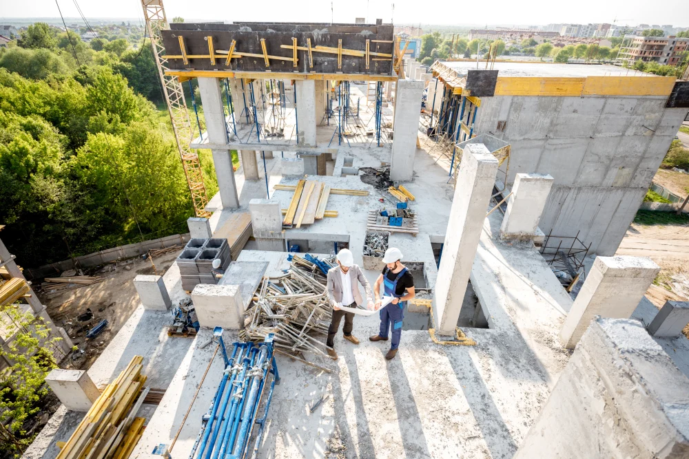 Vista a&eacute;rea de dos profesionales revisando planos en una obra en construcci&oacute;n