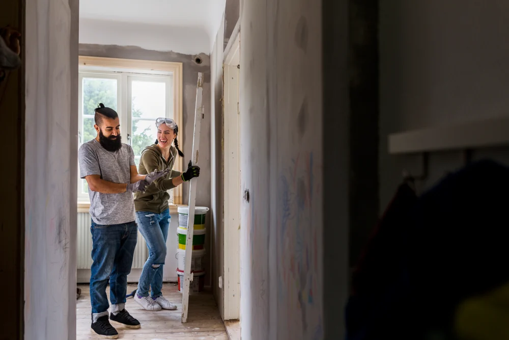 Pareja riendo mientras remodela una habitaci&oacute;n de su casa