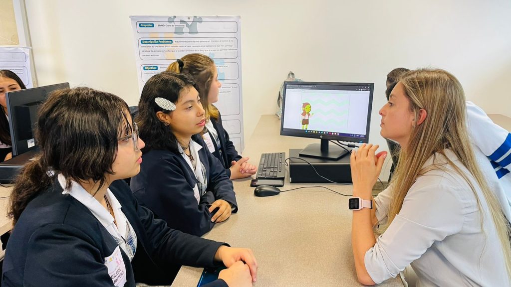 Jóvenes en computador hacen sus trabajos con una profesora